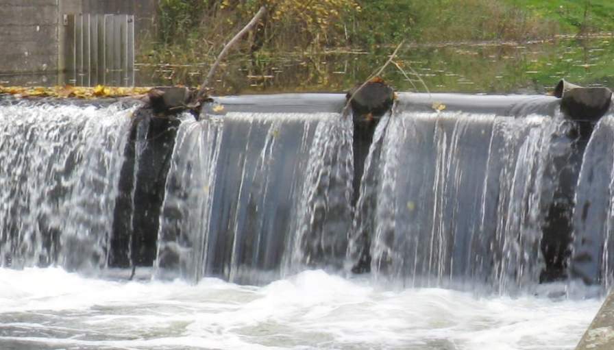 Fig. 2: Water flowing over a weir. Before the obstacle calm and slow, from the weir significantly faster; Source: Wikipedia
